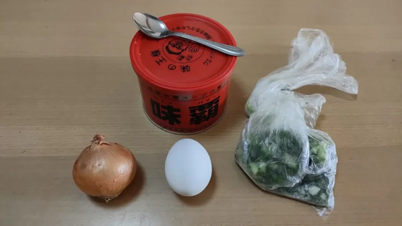 玉ねぎ、卵、透明の袋に入った小口ネギ、味覇、ティースプーンがテーブルの上に乗っている画像