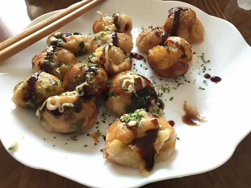 白い皿に盛り付けられた手作りのたこ焼きの写真。ソース、マヨネーズ、青のりがかかっており、左上には木製のお箸が添えられている。